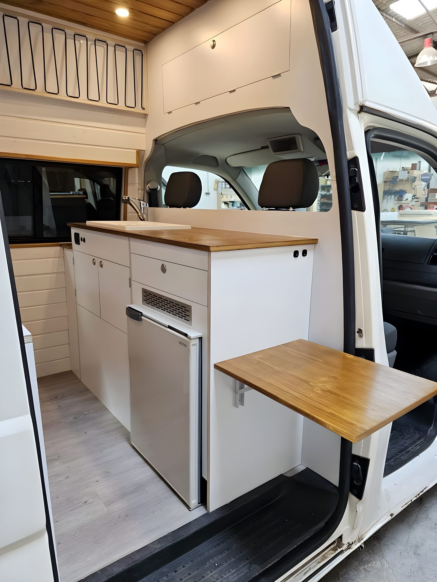 Interior de una camper con cocina, encimera de madera y armarios altos