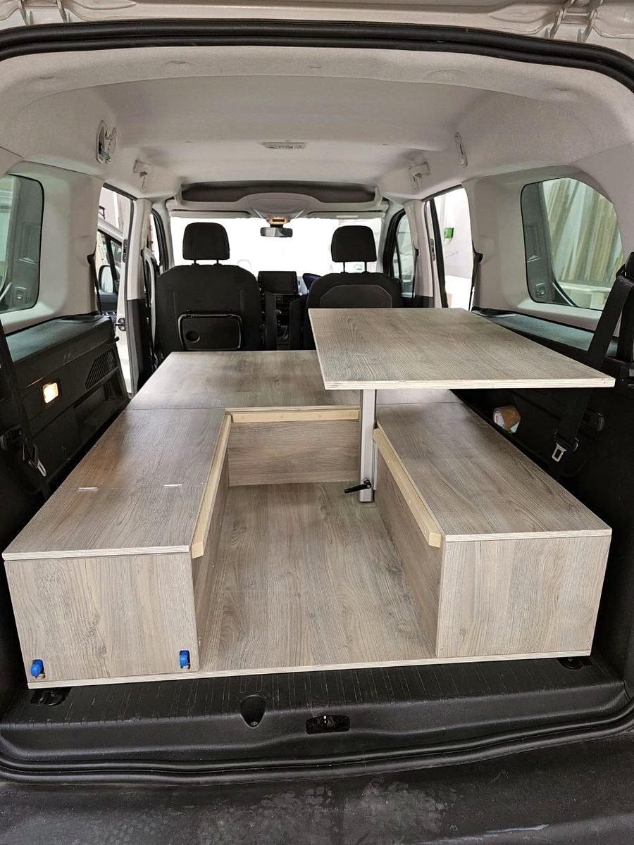 Interior de una camper con mesa central y bancos convertibles en cama