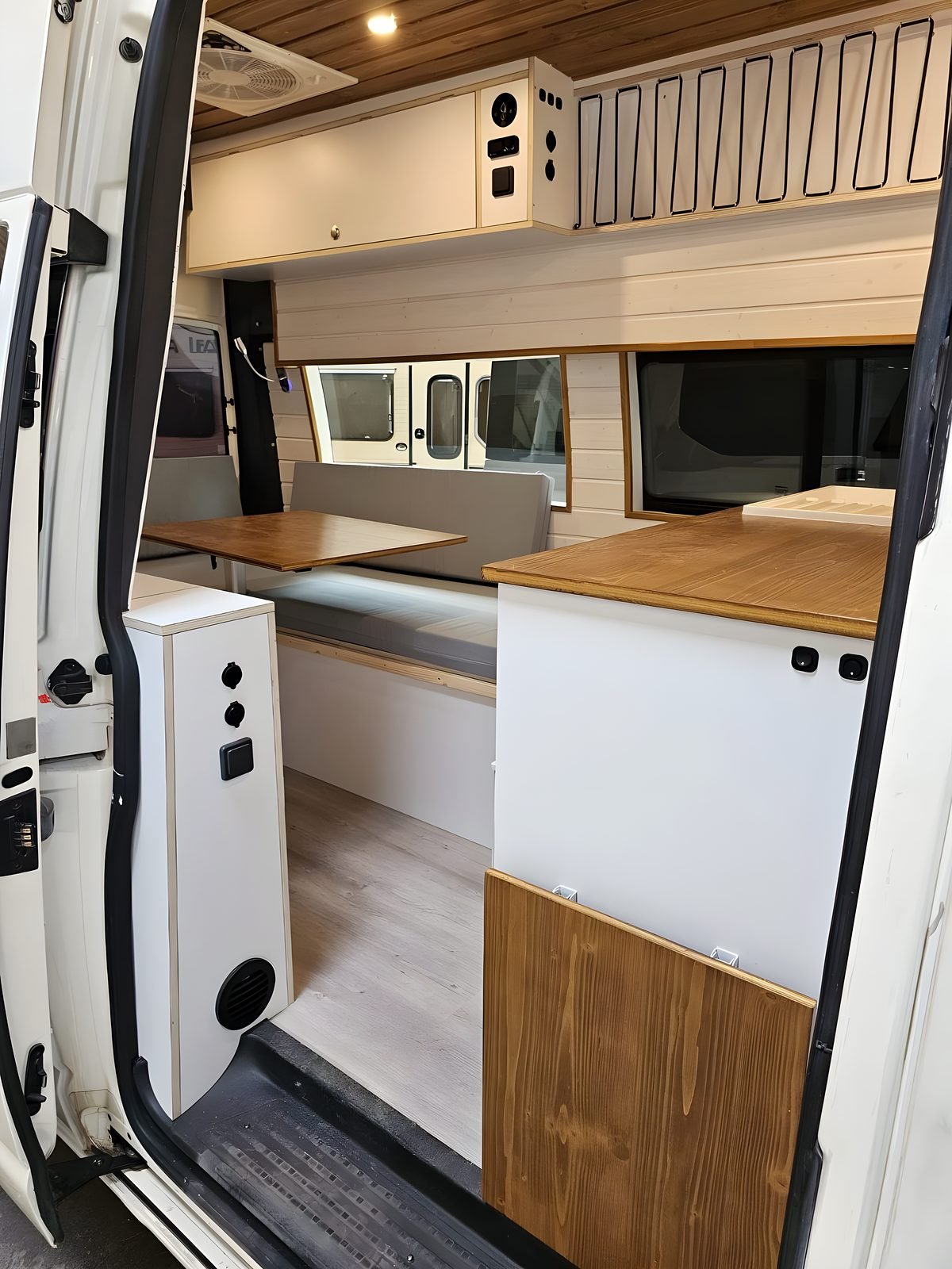 Interior de una camper terminada con cocina, nevera y encimera de madera